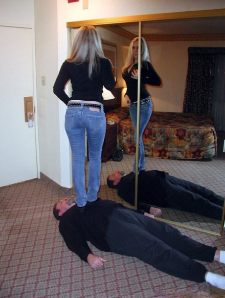 Fully clothed woman takes off her boots while trampling a man in sock feet 95744902